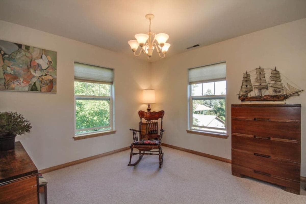 Interior view of room with two windows, rocking chair, dresser with ship model, and abstract art.