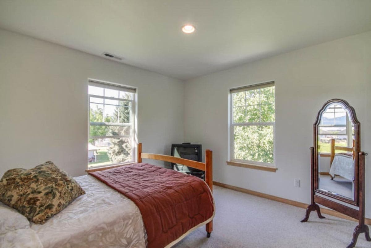 Bedroom with two windows, bed, television, and full-length mirror.