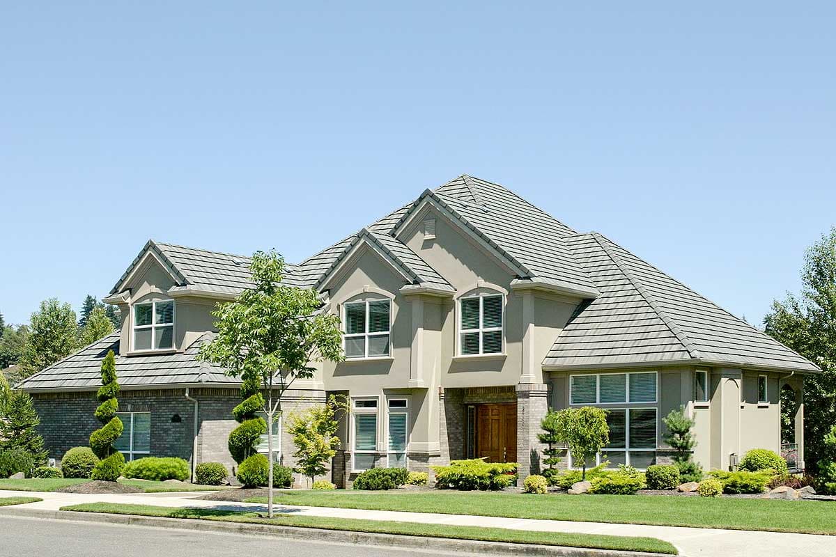 House plan exterior. Two-story home with a gabled roof, brick accents, and multiple dormers. Features a covered entry and manicured landscaping.