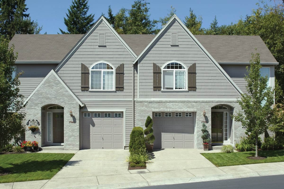 House plan exterior, two stories, side-by-side units with arched entryways, two garages, gabled roofs, and arched windows with shutters.