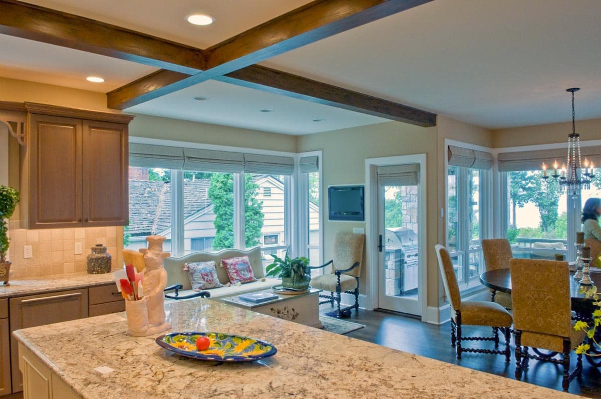Open-concept living area with kitchen, dining, and great room featuring coffered beams, large windows, and outdoor access.