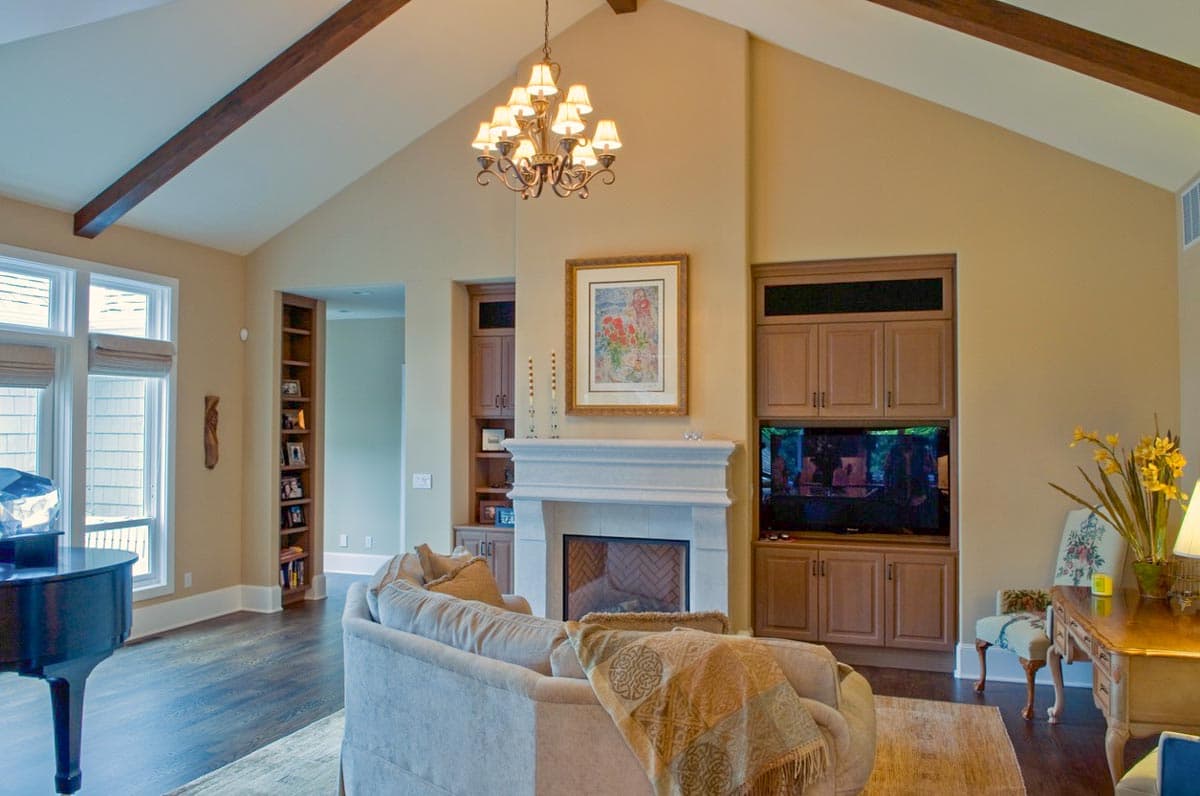 Great room with vaulted ceiling, exposed beams, stone fireplace, built-in entertainment center, and piano.