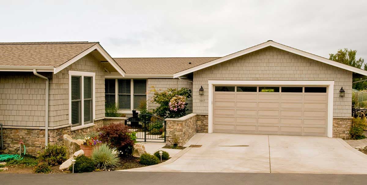 House plan exterior: single-story home with shake siding, stone foundation, and a two-car garage with a transom window.