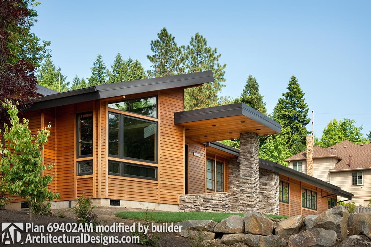 Modern house plan exterior with wood siding, flat roof, stone column entry, and large picture windows.