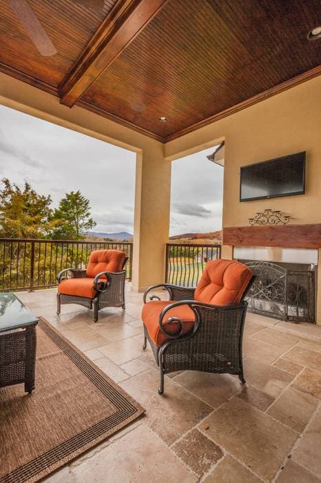 Covered patio with wood ceiling, seating area, outdoor fireplace, and mountain views.