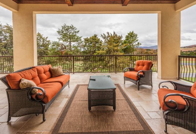 Covered outdoor living space with seating area, tiled floor, and view of trees and hills.