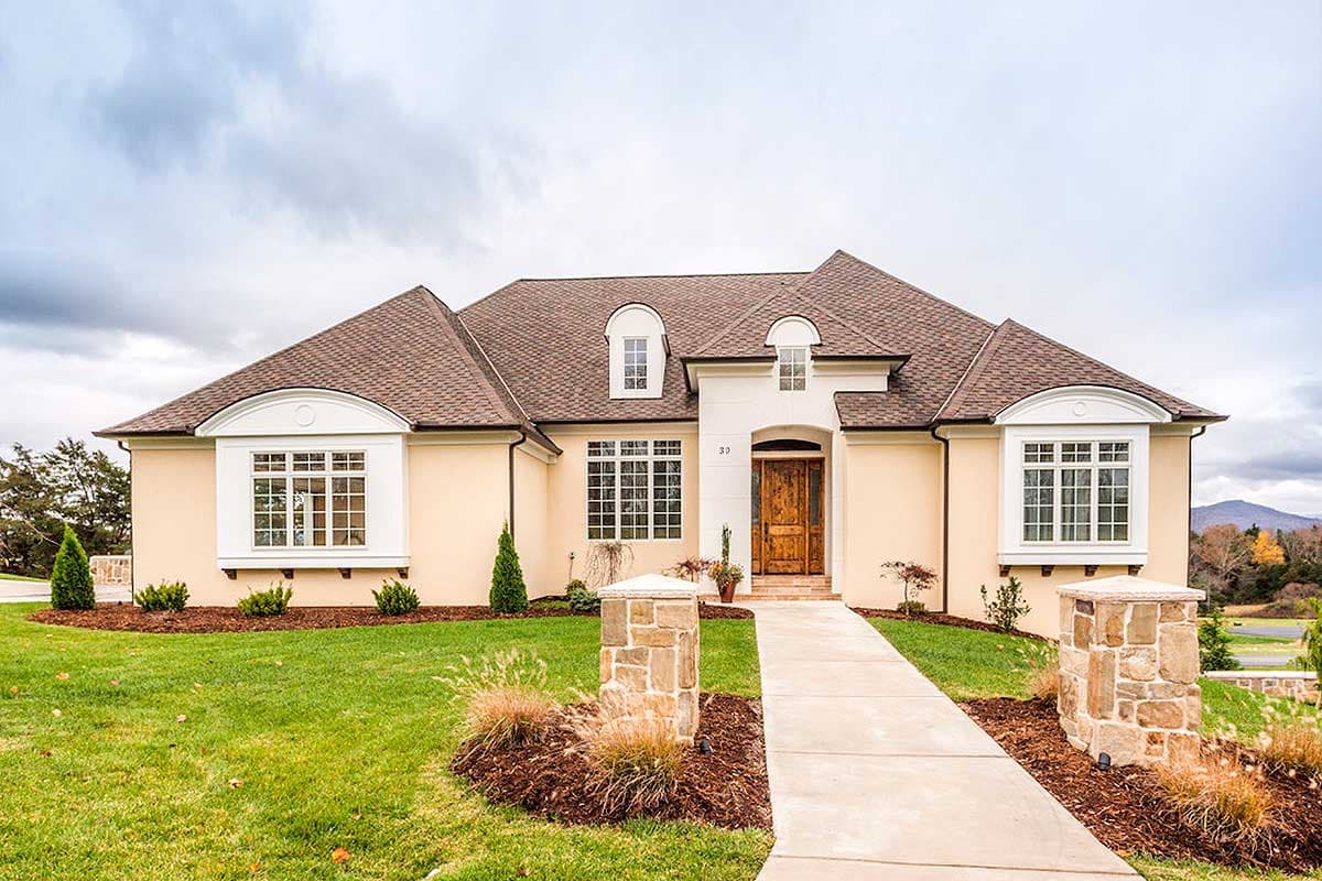 House plan exterior featuring a two-story home with a gabled roof, arched window surrounds, and dormers. Includes a stone walkway and pillars.