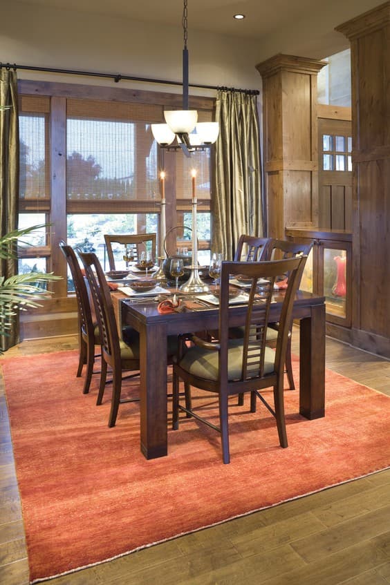 Dining room with dark wood table and chairs on an orange rug, set with place settings.