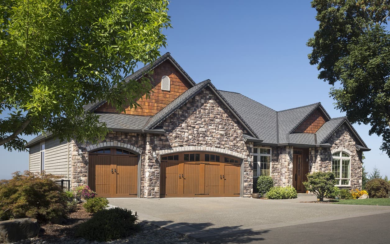 House plan exterior with stone and wood siding, prominent gables, and two arched garage doors.