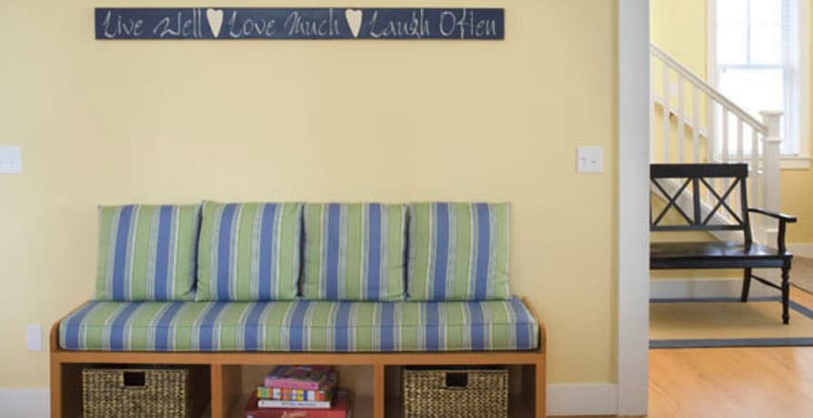 Entryway bench with striped cushions, storage cubbies, and decorative wall sign near staircase with dark bench.