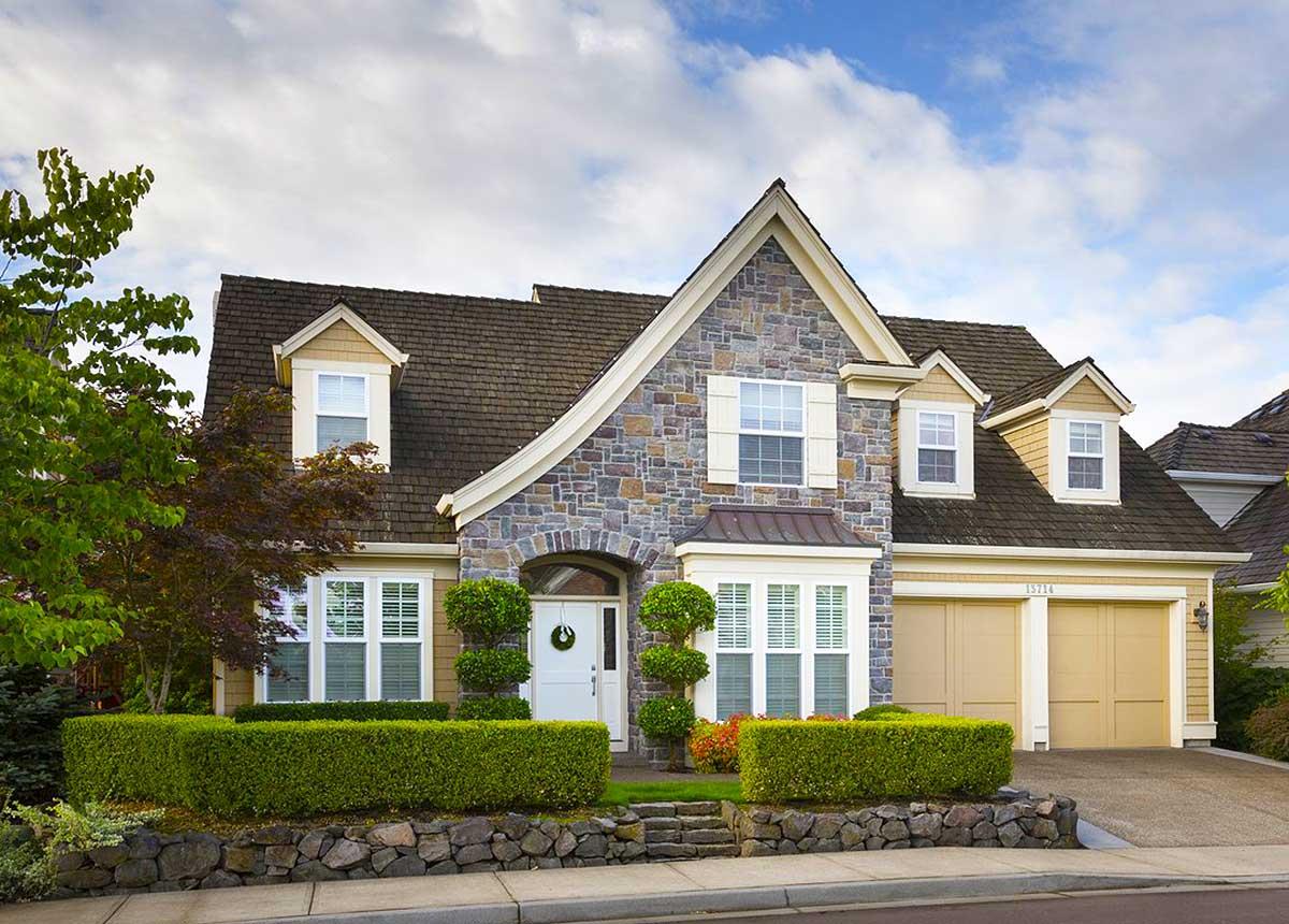 House plan exterior: Two-story home with stone facade, arched entryway, bay window, dormers, and a three-car garage.