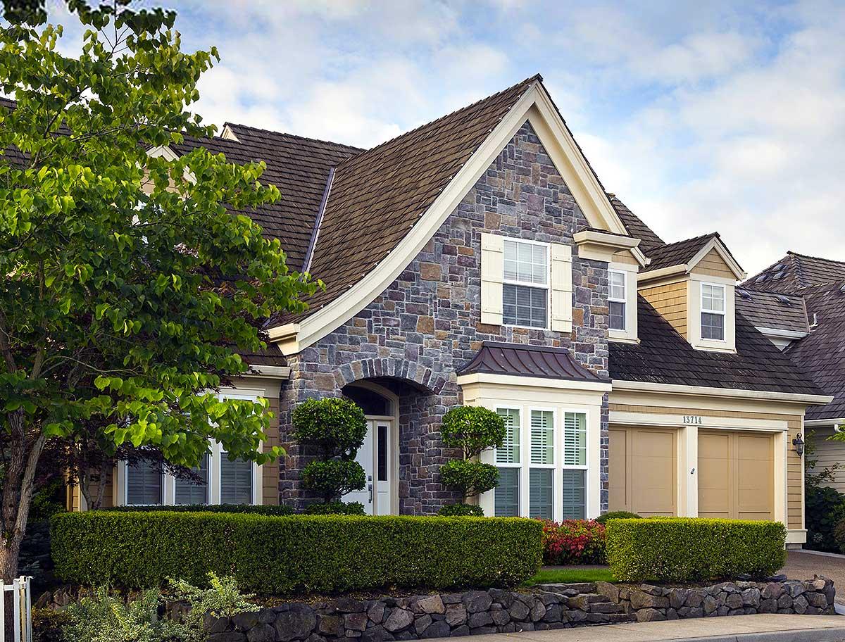 House plan exterior with stone facade, arched entryway, bay window, dormers, and attached two-car garage.