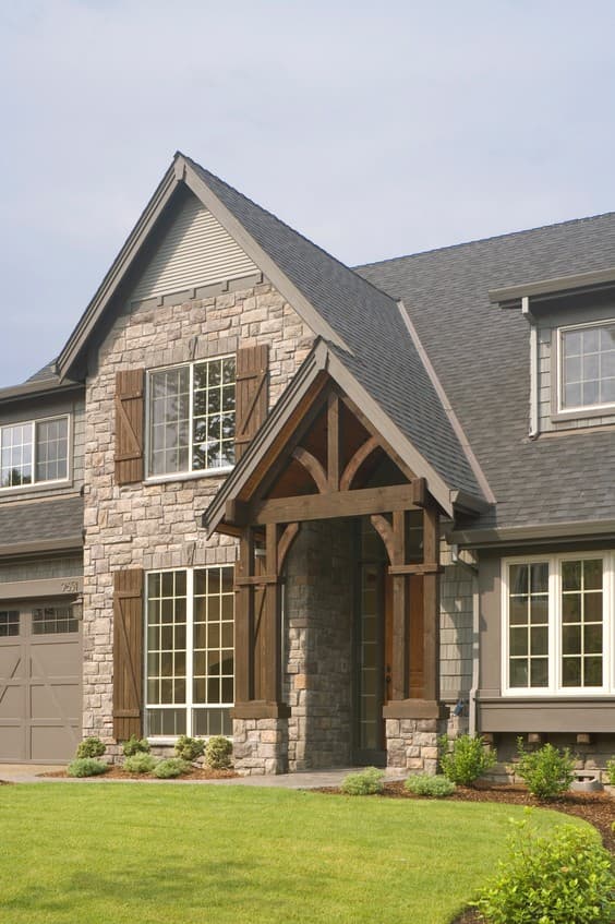 House plan exterior featuring stone facade, prominent wood-accented gable entrance, large grid windows, and attached garage.