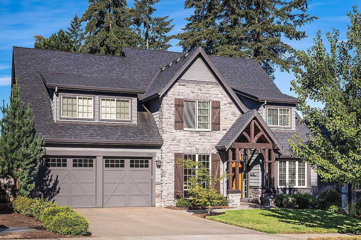 House plan exterior: Stone and shingle siding, dual garage doors, gabled dormers, and timber-frame entry.