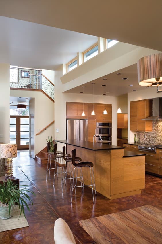 Modern kitchen with central island, stainless steel appliances, and wood cabinetry. Staircase with decorative railing visible.