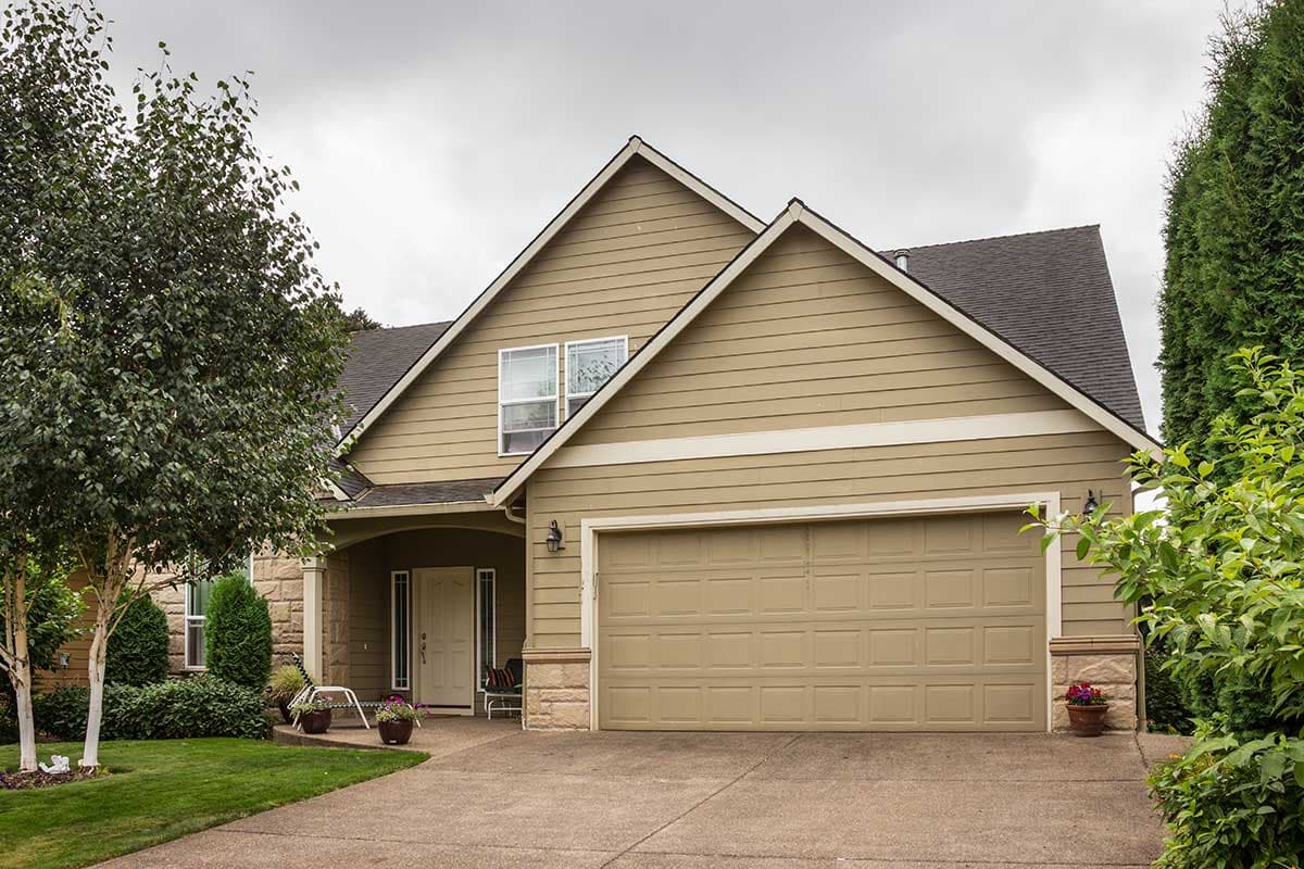 House plan exterior: tan siding, two-story, gabled roof, covered porch, and attached two-car garage.