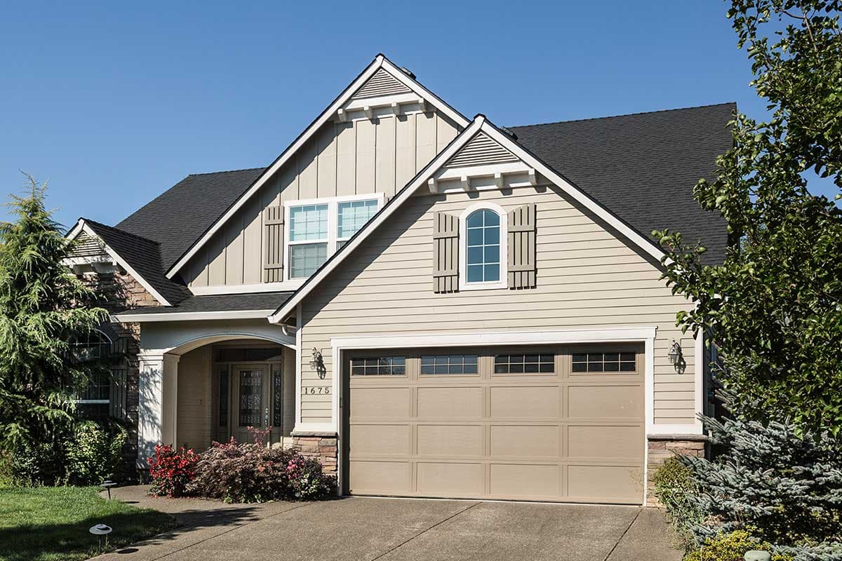 House plan exterior: Two-story home with siding, stone accents, gable dormers, arched window, and a two-car garage.