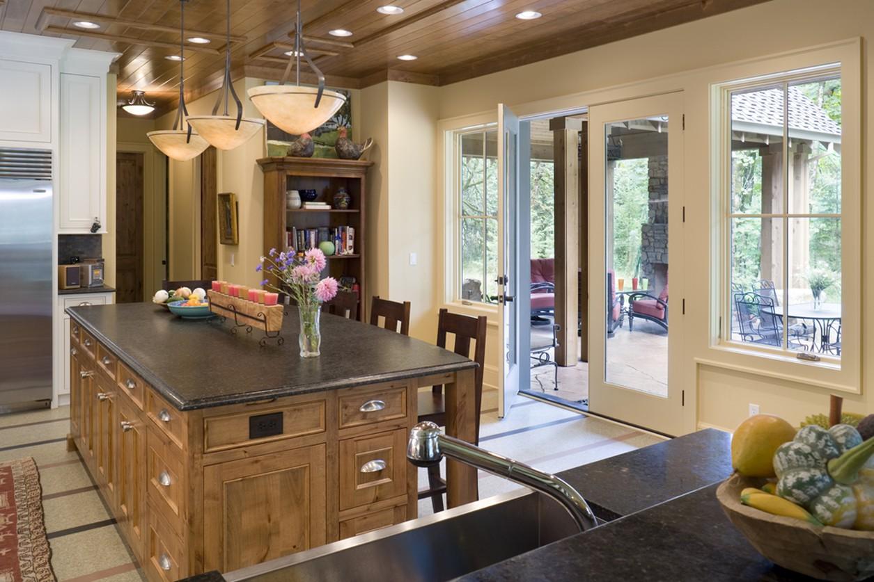 Kitchen with large wood island, granite countertops, pendant lights, and double glass doors opening to a covered patio.