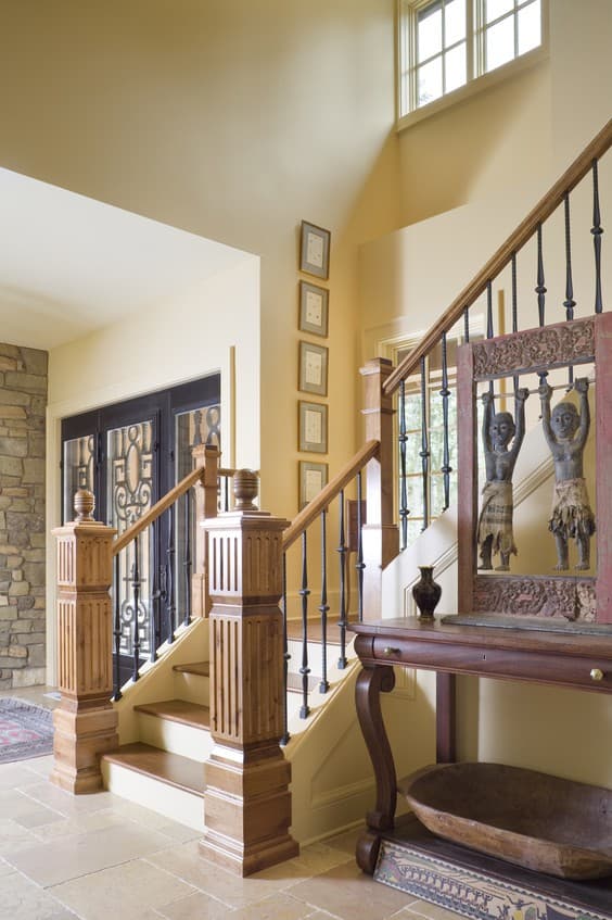 Interior view of a two-story foyer with a grand staircase, decorative newel posts, wrought iron balusters, and a stone accent wall.