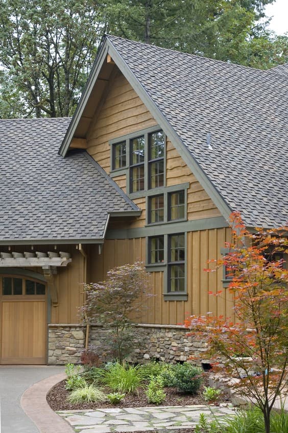 Craftsman style house exterior with wood siding, stone foundation, and stacked windows on a steeply pitched roofline.