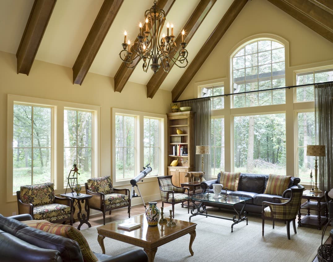 Living room interior with vaulted ceiling, exposed wood beams, large windows, and traditional furnishings.