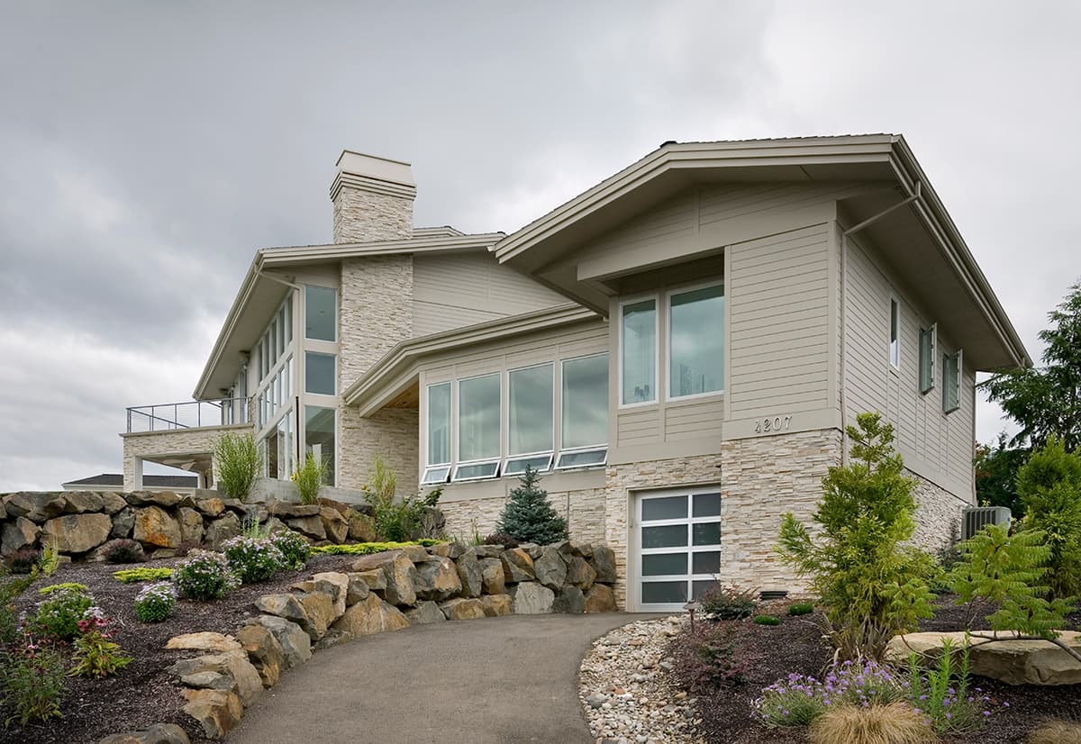 Modern house plan exterior with stone accents, multi-level rooflines, large windows, and a glass garage door.