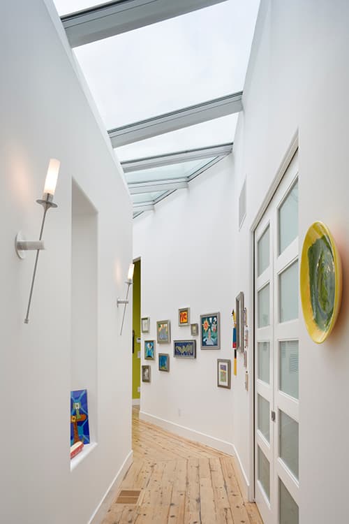 Hallway interior with pitched skylight, modern sconces, artwork, and paneled doors.