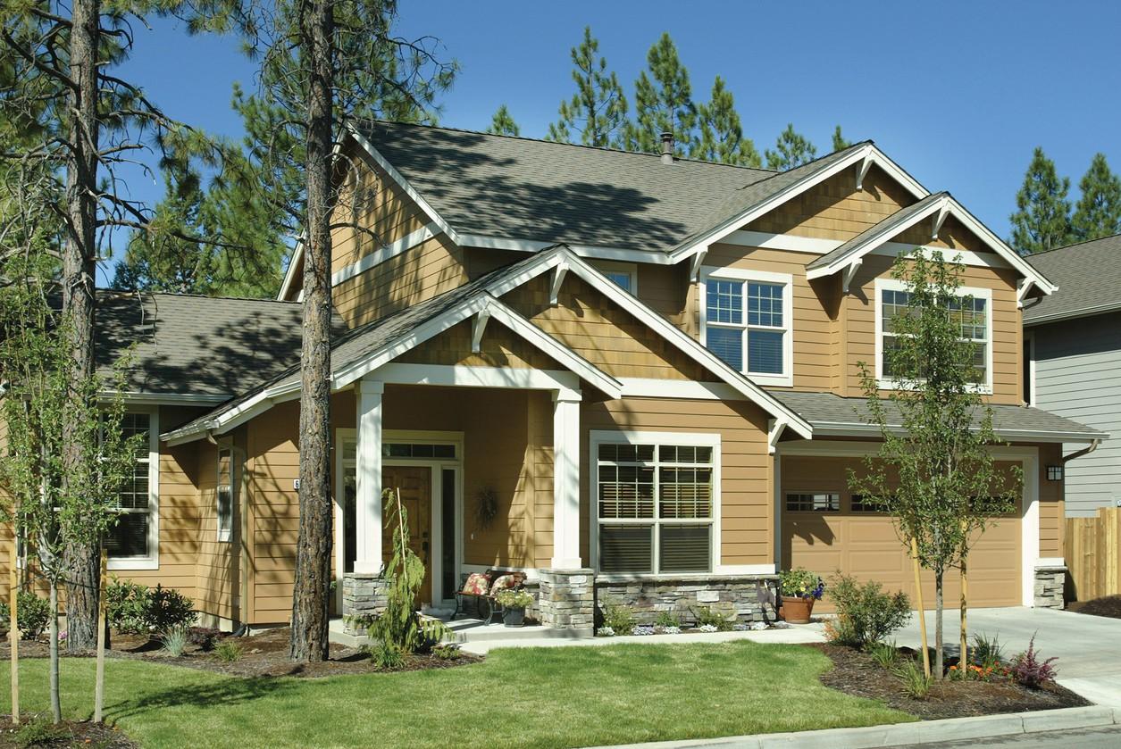 Two-story house plan exterior with prominent gables, covered porch with stone-clad columns, and two-car garage.