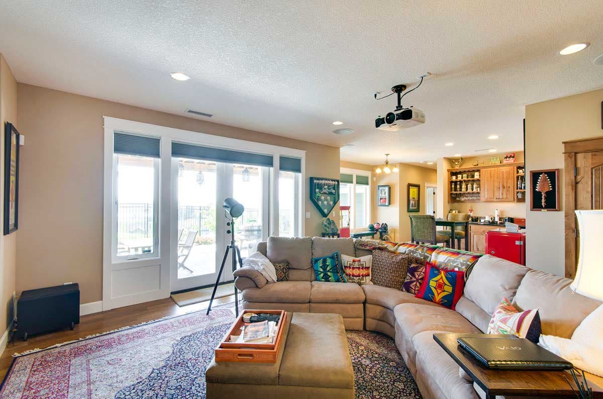 Living room with large sectional sofa, patterned pillows, projector, and view of a kitchen and bar area.