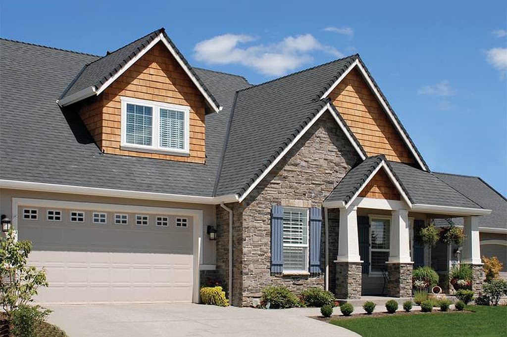 House plan exterior with stone facade, wood shingle gables, dormer window, and attached garage.