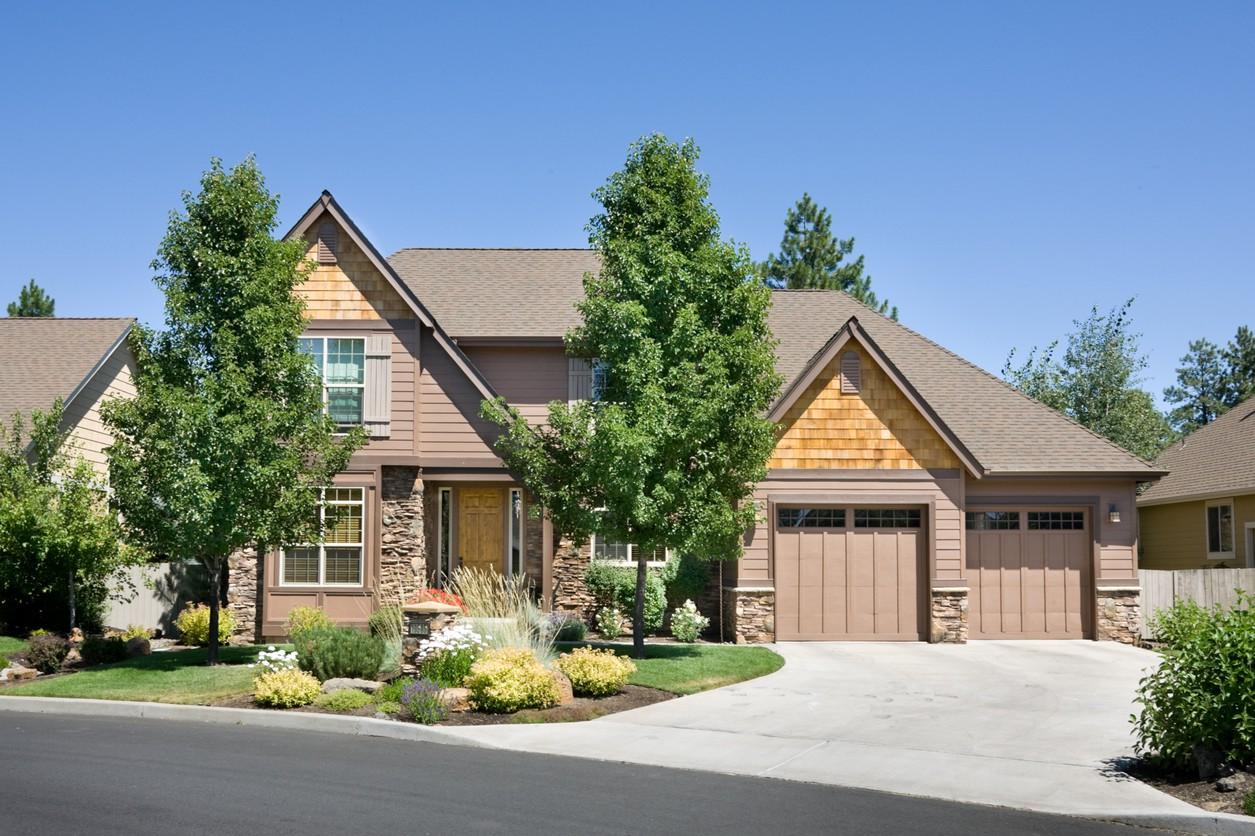 House plan exterior: Two-story home with prominent gables, cedar shake siding accents, stone foundation, and a three-car garage.
