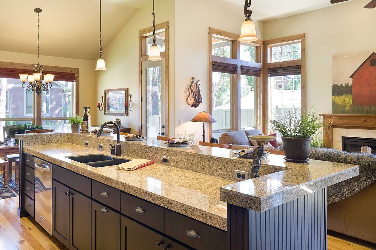Open-concept kitchen with granite countertops, a large island with sink, dark wood cabinets, and vaulted ceiling.