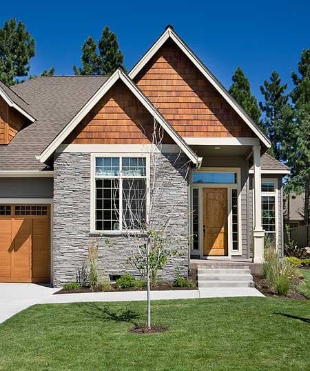 House plan exterior with stacked stone, wood shingle gables, wood front door, and two-car garage.