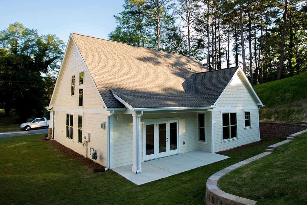 House plan exterior: Gable roof, siding, porch with French doors, and multiple windows on a sloped lot.