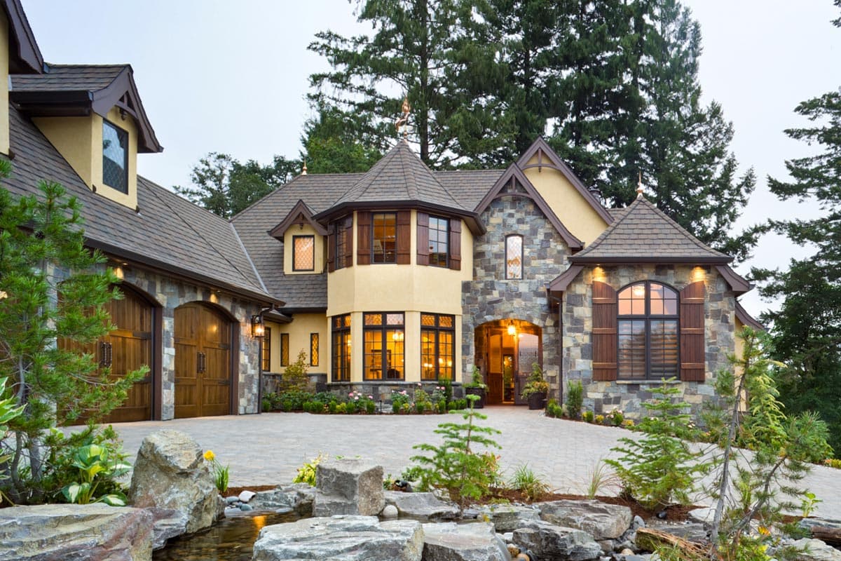 House plan exterior featuring stone and stucco, multiple gables, arched wood garage doors, and decorative window shutters.