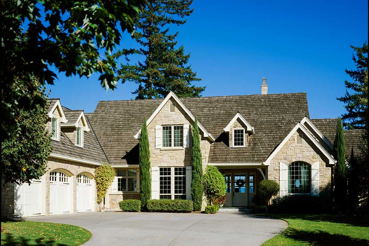 House plan exterior with stone facade, steeply pitched roof, dormers, and three-car garage.