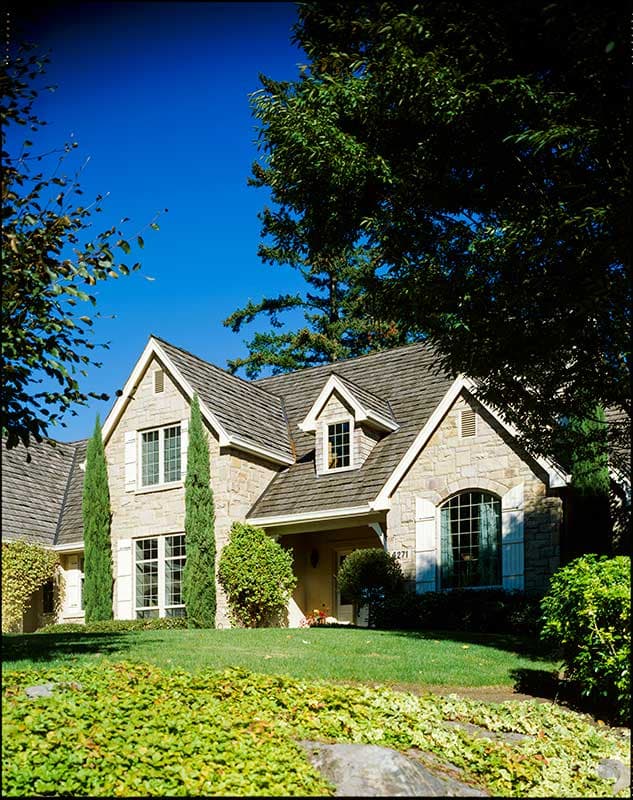 House plan exterior: Stone-clad two-story home with multiple gables, dormer window, and covered entry.