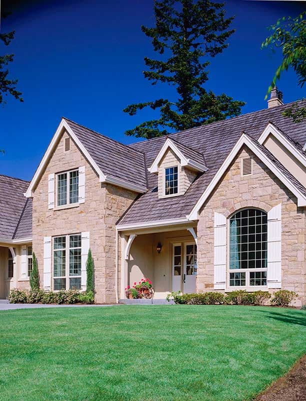 House plan exterior featuring stone facade, arched window, dormers, and covered entry with white shutters.