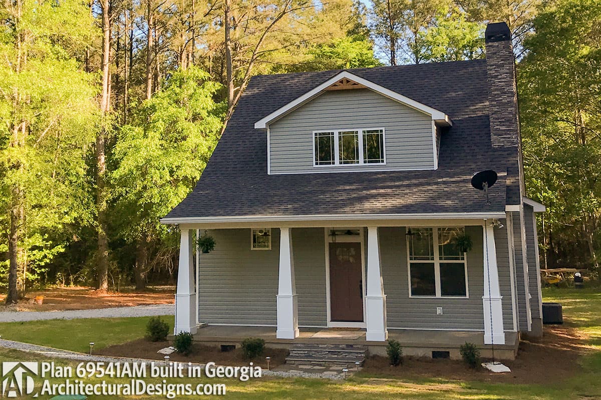 House plan exterior: Two-story home with prominent stone chimney, front porch with square columns, and dormer window.