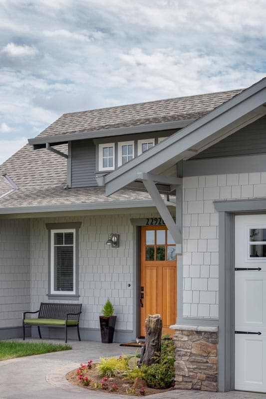 House plan exterior with a gabled dormer, wood front door, and stone accents on the garage.