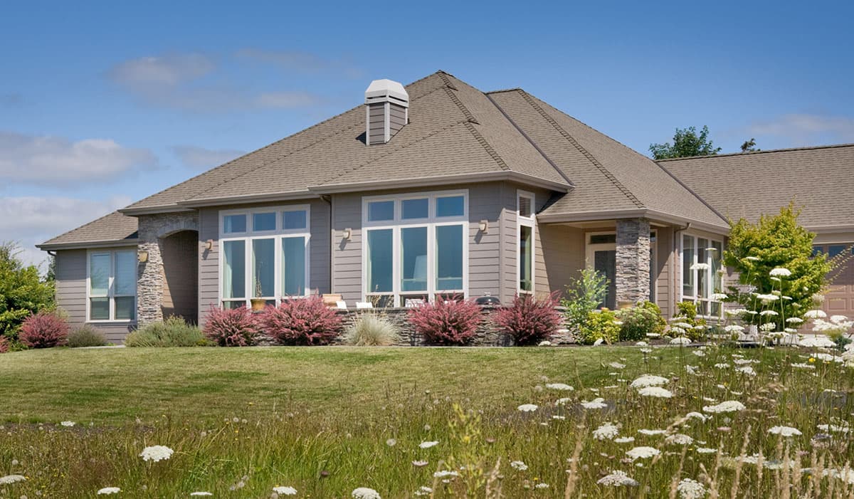 House plan exterior: Single-story home with stone accents, multiple large windows, gabled roof, and prominent chimney.