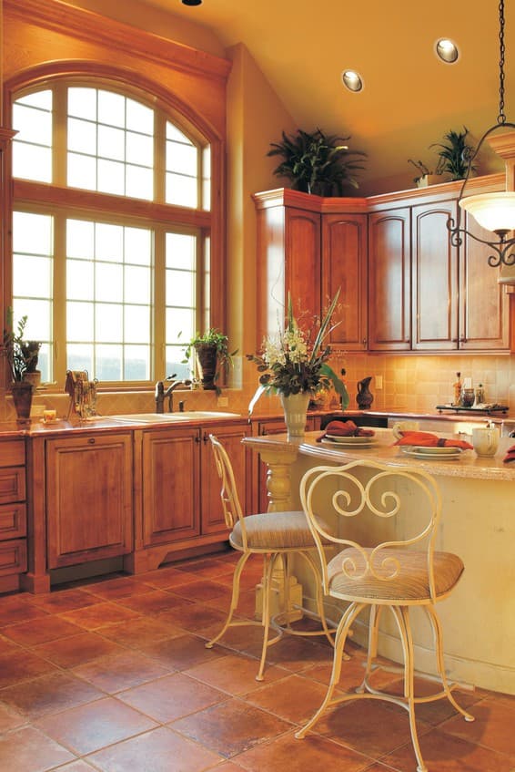 Kitchen with arched window, wood cabinetry, island with seating, and tile flooring.