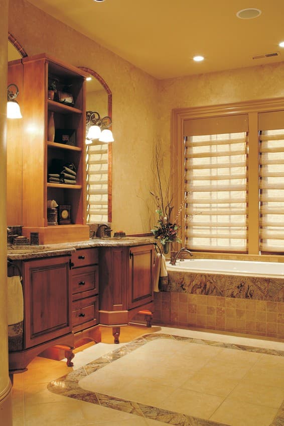Bathroom with wood vanity, granite countertop, soaking tub, tiled wainscoting, and decorative flooring.