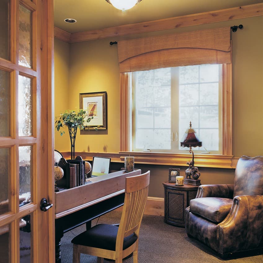 Home office with paneled glass doors, desk with books and laptop, leather armchair, and large grid window.