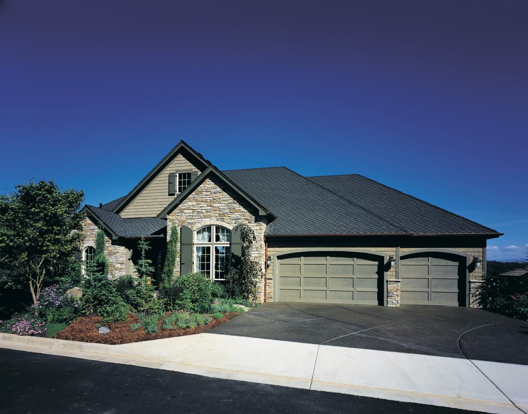 House plan exterior with stone accents, arched window, dormer, and a three-car garage with arched doors.