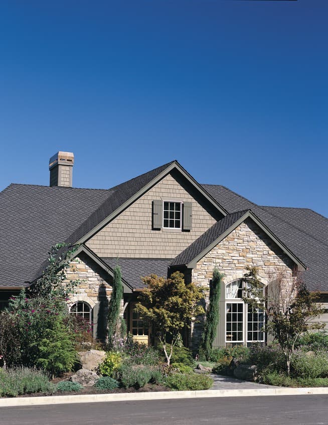House plan exterior: Two-story home with stone and shingle facade, gabled roof, dormer window, and arched entryway.