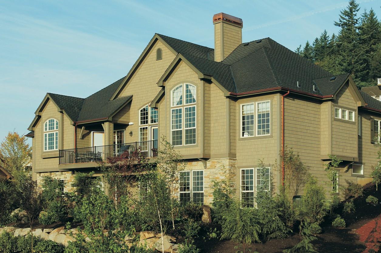 House plan exterior: Two-story home with gable dormers, arched windows, stone base, and a large deck.