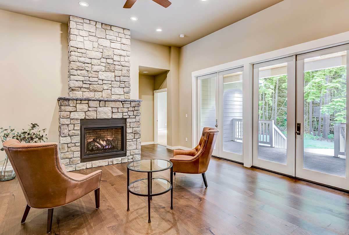 Living room interior with stone fireplace, two leather chairs, glass side table, and sliding glass doors leading to deck.