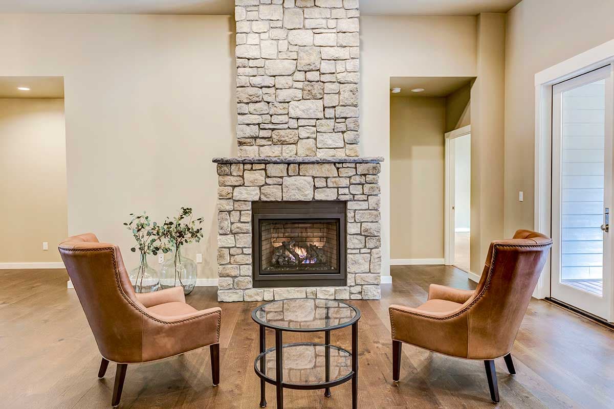 Living room with stone fireplace, glass-top coffee table, and two leather chairs.