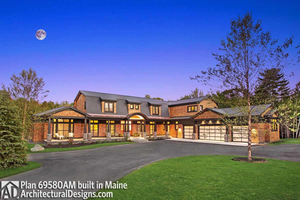 House plan exterior. Two-story with cedar shingle siding, covered porch, multiple dormers, and attached garage with glass doors.